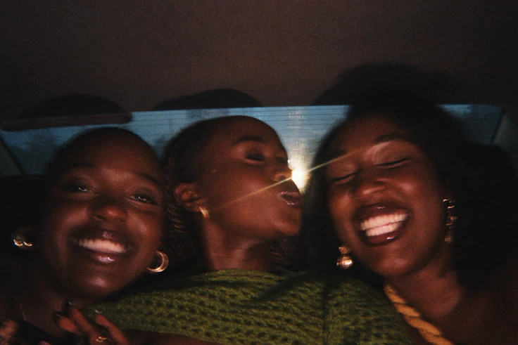 Three young Black women laughing together in a car at night.